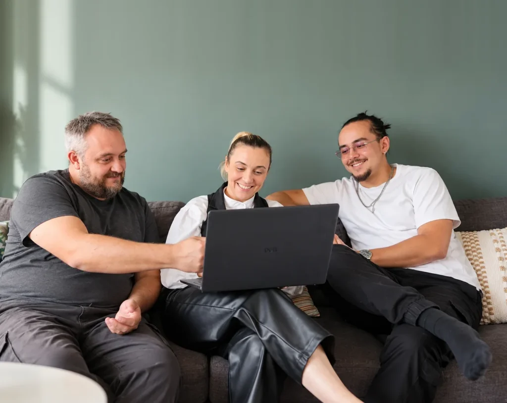 Cédric Huet, Maïté Kindts et Noham Chaveneau, souriants, échangent autour d'un ordinateur portable sur le canapé du cabinet