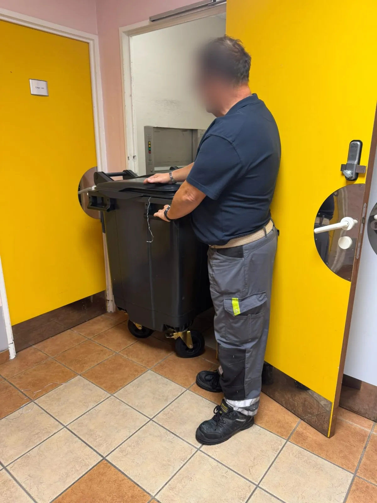 Agent de service déplaçant un conteneur de linge dans un établissement de santé
